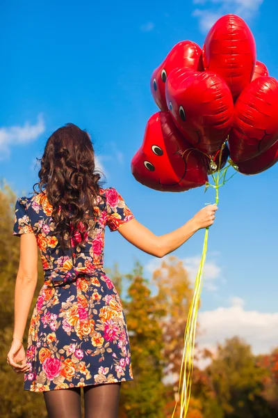 Rückansicht einer jungen Frau mit roten Luftballons in der Hand — Stockfoto