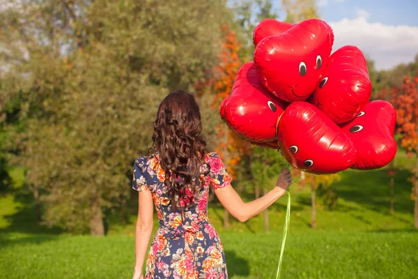 Rückansicht einer jungen Frau mit roten lächelnden Luftballons in der Hand — Stockfoto