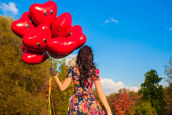 Rückansicht der attraktiven jungen Frau mit roten lächelnden Luftballons in der Hand im Freien — Stockfoto