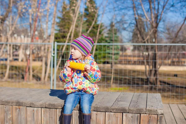 暖かい春の日には公園でトウモロコシを食べる小さな愛らしい女の子 — ストック写真