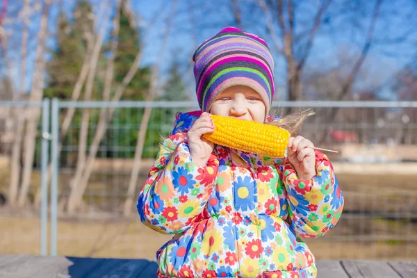 Gadis kecil menggemaskan makan jagung di taman pada hari musim semi yang hangat — Stok Foto