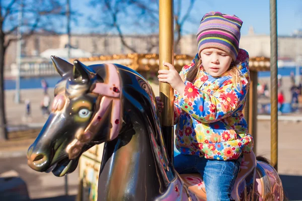 Pequena menina feliz montando no carrossel em um parque de diversões — Fotografia de Stock