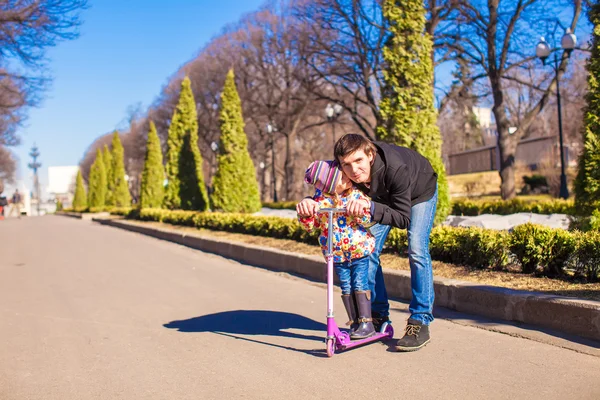 Adorable little girl and happy father ride on scooter at sunny day — Stock Photo, Image