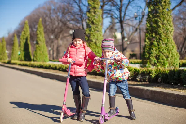 Schattige kleine zusters rijden scooters op een warme zonnige lente — Stockfoto