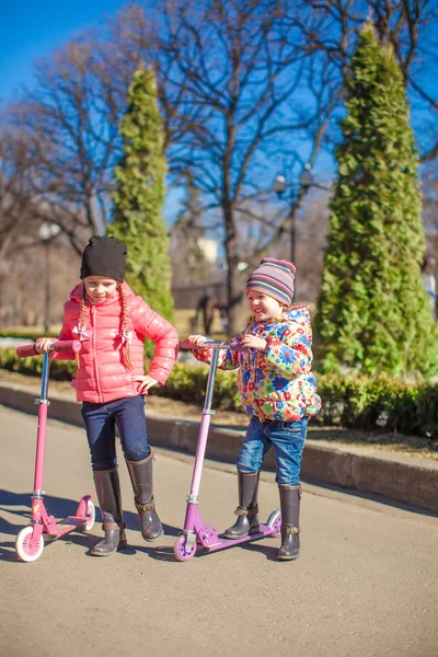 Little adorable girls with scooter in spring park at warm day — Stock Photo, Image