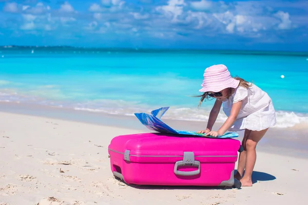 Little adorable girl with big colorful suitcase and a map in hands on tropical beach — Stock Photo, Image