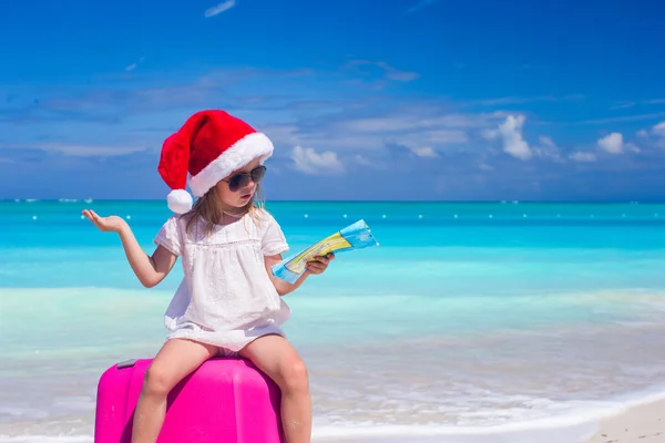 Klein meisje bij santa hat zittend op een grote koffer met kaart in handen — Stockfoto