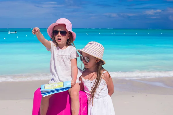 Urocza dziewczynka, patrząc na sposób mapę i duża walizka na plaży — Zdjęcie stockowe