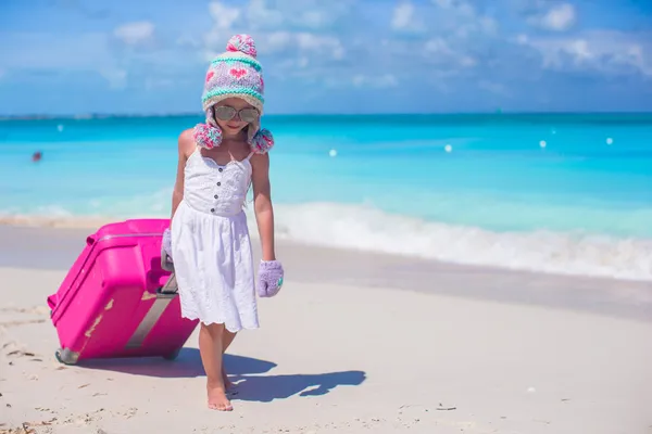 Adorable girl in warm winter hat and mittens walking with luggage on beach — Stock Photo, Image