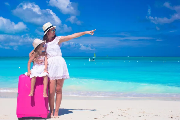 Young mother and her little daughter with luggage on tropical white beach — Stock Photo, Image