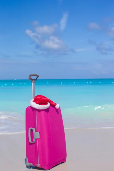 Closeup of pink suitcase and Santa Claus hat background the sea — Stock Photo, Image