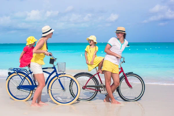 Young family of four riding bicycles on a tropical sand beach — Stock Photo, Image
