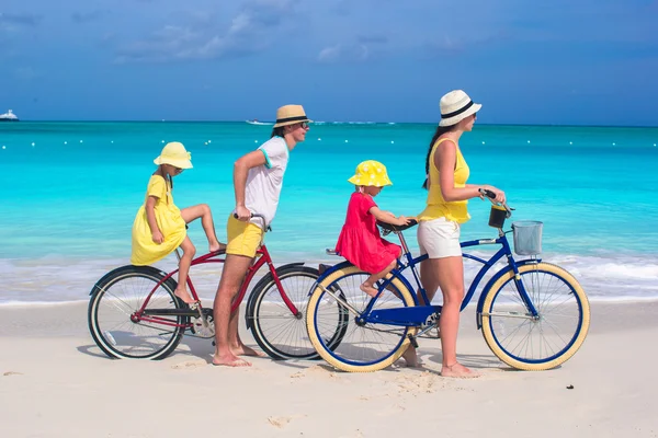 Giovani genitori e bambini in sella a biciclette su una spiaggia tropicale di sabbia bianca — ストック写真