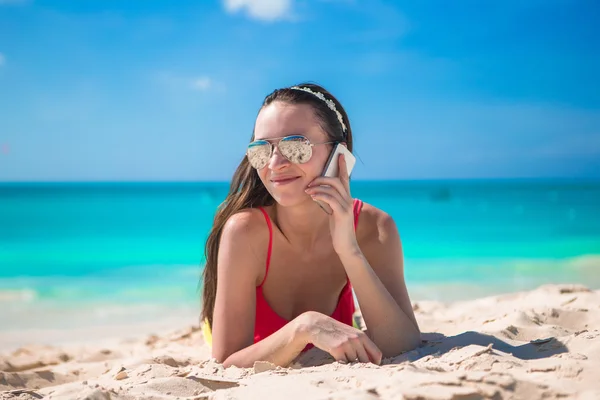 Jonge vrouw liggend op wit zand en praten door haar telefoon — Stockfoto