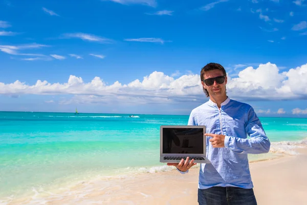 Young man with laptop on the background of turquoise ocean at tropical beach — Stock Photo, Image