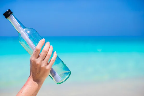 Flaska med ett meddelande i hand bakgrunden blå himlen — Stockfoto