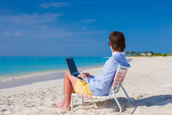 Jeune homme utilisant un ordinateur portable sur la plage tropicale — Photo