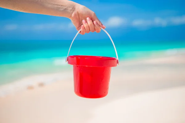 Nära håll handen håller en liten röd hink på tropisk strand — Stockfoto