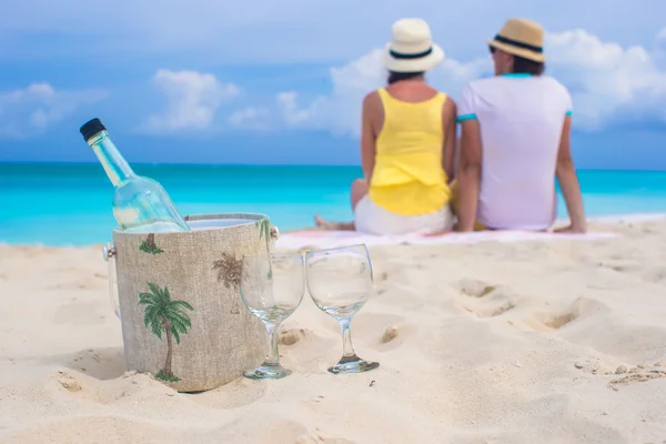 Bottle of white wine and two glasses background happy couple on sandy beach — Stock Photo, Image