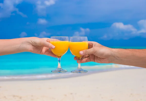 Due mani tengono bicchieri con succo d'arancia sfondo cielo blu — Foto Stock