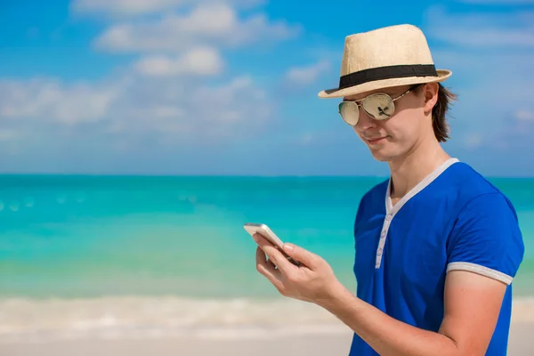 Młody człowiek zadowolony z jego telefonu na wakacje na plaży — Zdjęcie stockowe