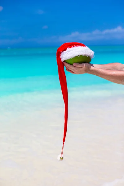 Coconut with Santa hat in male hands against the turquoise sea — Stock Photo, Image