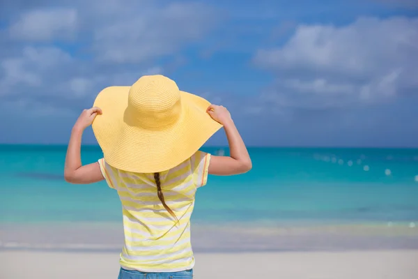 Achteraanzicht van meisje in een grote gele stro hoed op wit zand strand — Stockfoto