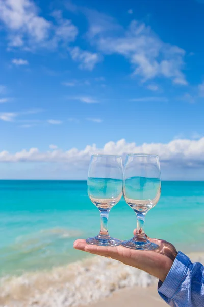 Closeup of two wineglasses in a man's hand on the white sandy beach — Stock Photo, Image