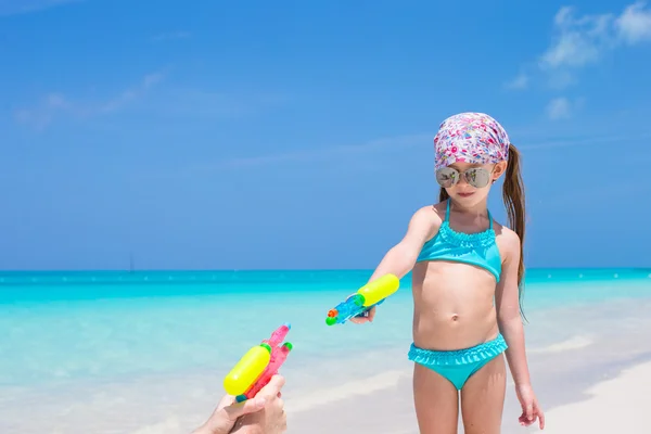 Liten flicka spelar med vatten pistol på tropical beach — Stockfoto