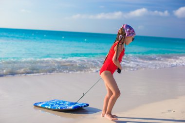 küçük sevimli kız bir sörf tahtası beyaz kıyıya çeker.