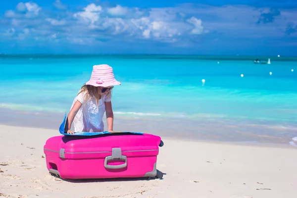 Little adorable girl with big colorful suitcase and a map on tropical beach — Stock Photo, Image