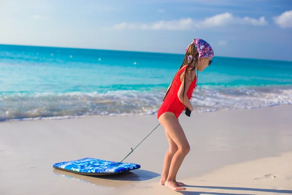 Kleines entzückendes Mädchen zieht Surfbrett am weißen Ufer — Stockfoto