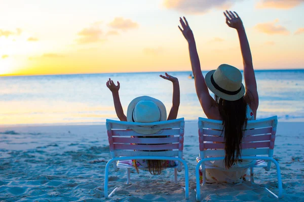 Klein meisje en moeder zittend op het strandstoelen bij zonsondergang — Stockfoto