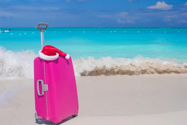 Närbild av rosa bagage och jultomten hatt på tropisk strand — Stockfoto
