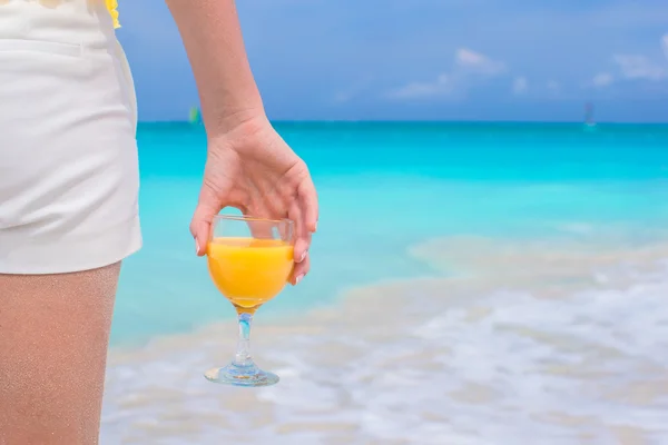 Närbild orange juice i en kvinnlig hand på bakgrund av havet — Stockfoto