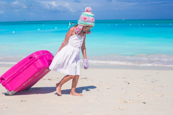 Schattig meisje in winter muts en wanten wandelen met bagage op strand — Stockfoto