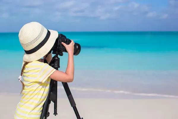 Little girl with camera on a tripod at white sandy beach — Stock Photo, Image