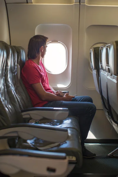 Young man looking in window on board of an airplane during the flight — Stock Photo, Image