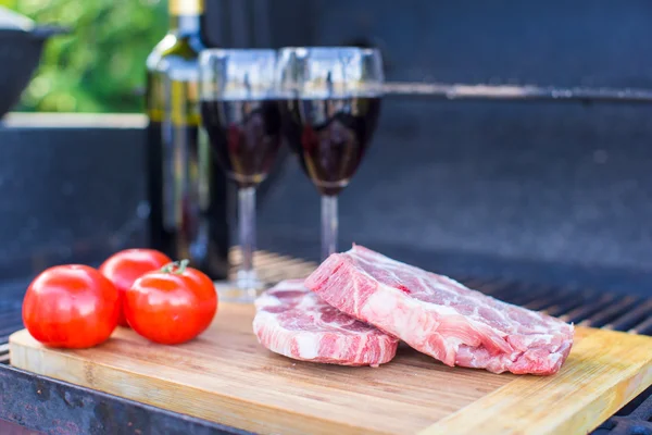 Dos copas de vino tinto, bistec y tomates en la barbacoa al aire libre — Foto de Stock