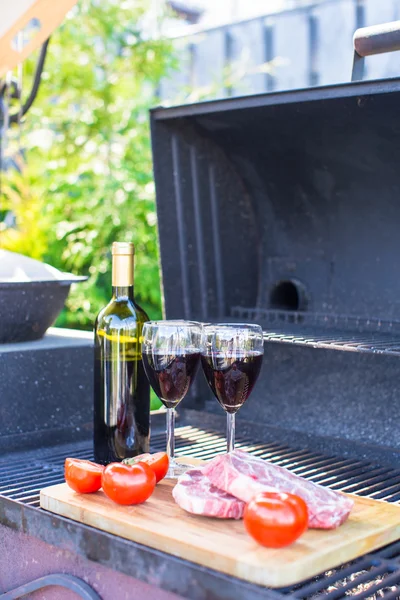 Bottle of red wine, steak and tomatoes on barbecue outdoors — Stock Photo, Image