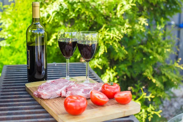 Two glass of red wine, steak and tomatoes on barbecue outdoors — Stock Photo, Image