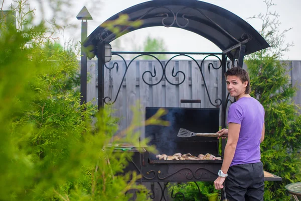 Молодий чоловік смажить стейки на грилі на відкритому повітрі у своєму дворі — стокове фото
