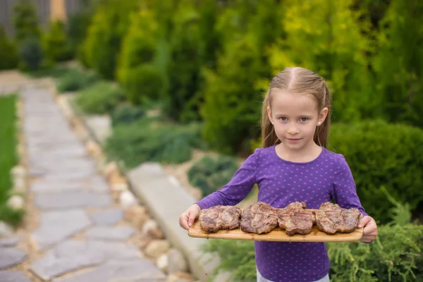 Adorable niña con filetes a la parrilla en las manos al aire libre —  Fotos de Stock