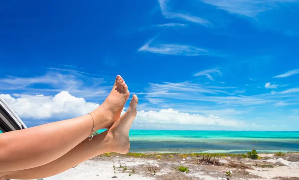 Vrouwelijke barefoot vanuit het venster van een auto op achtergrond tropisch strand — Stockfoto