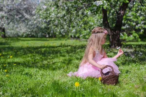Nettes kleines Mädchen pflückt Blumen im blühenden Apfelgarten am sonnigen Tag — Stockfoto