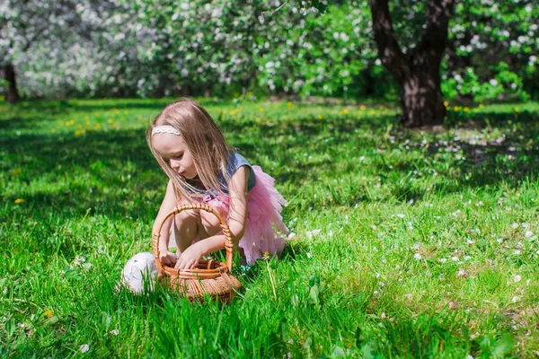 Bedårande liten flicka med halm korg i blommande äppelträdgård — Stockfoto