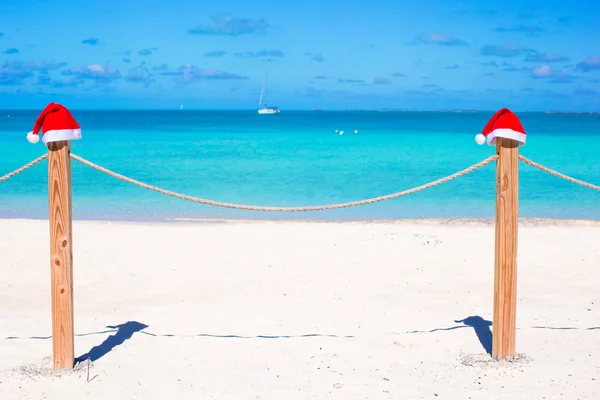 两个圣诞老人的帽子，在热带的白色沙滩的栅栏上 — 图库照片