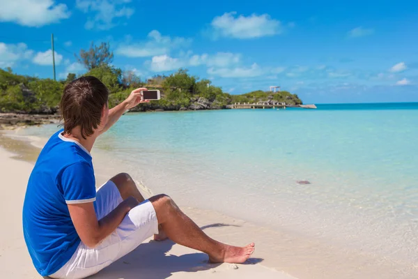Ung man i santa mössa med telefon på tropical caribbean beach — Stockfoto