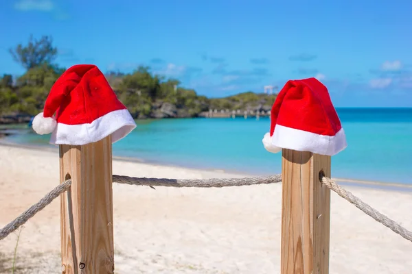 在热带的白色沙滩的栅栏上特写两个圣诞老人的帽子 — 图库照片