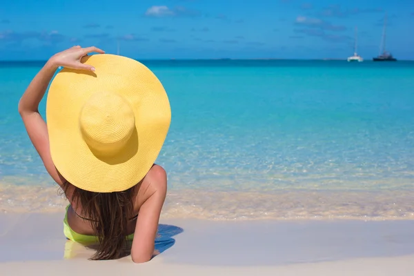 Woman sitting in yellow hat on white sand beach enjoying summer vacation — Stock Photo, Image